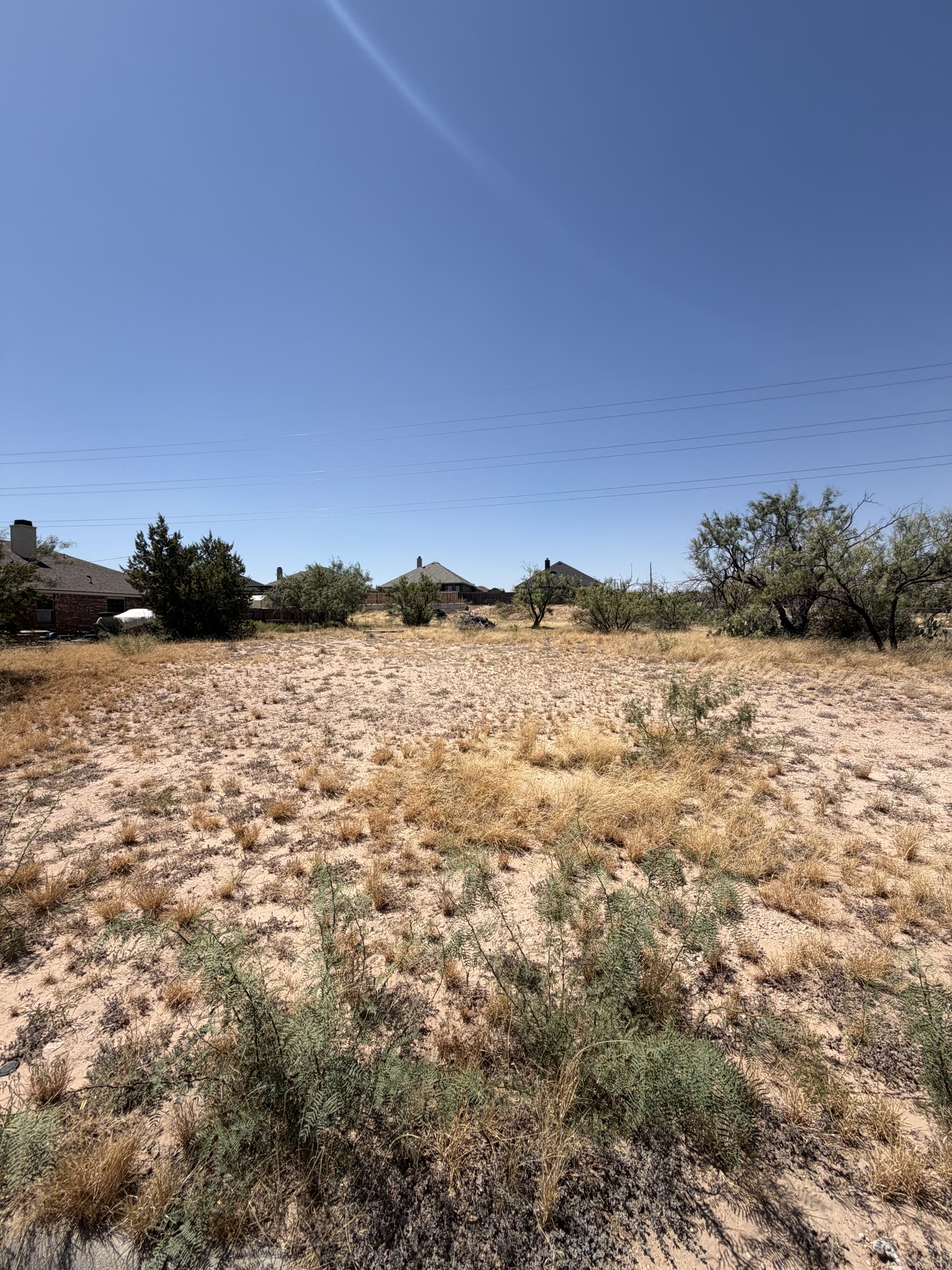 Vacant lot at 700 Baylor Blvd in Big Spring, Texas, seen from a high angle over sandy ground and mesquite shrubs